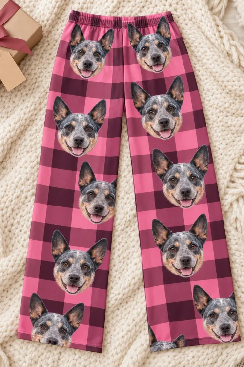 Pink plaid australian cattle dog pajama pants laid flat on a cream knit blanket beside a wrapped gift box