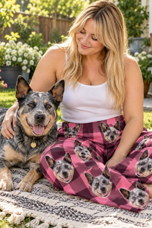 Woman petting a blue heeler on a garden picnic blanket, wearing pink plaid cattle dog pajamas with heeler faces