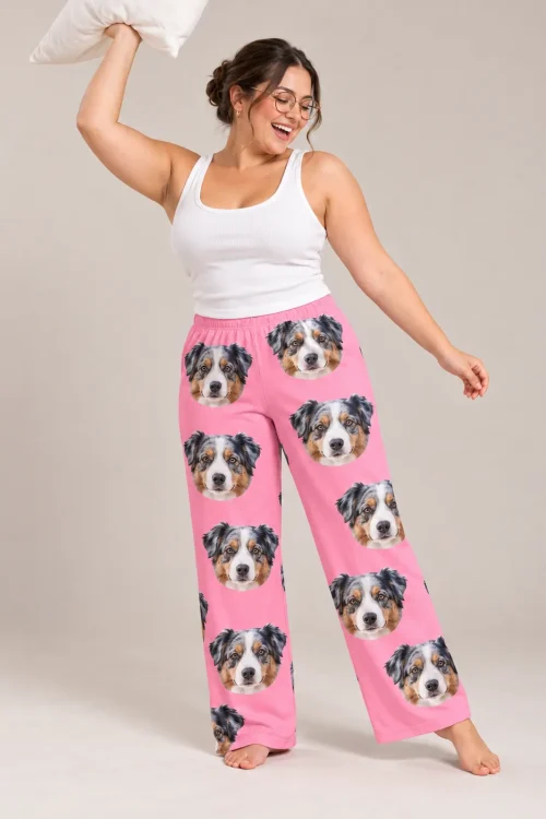 Woman laughing with a pillow raised overhead, in pink Australian shepherd pajama pants against a soft gray studio