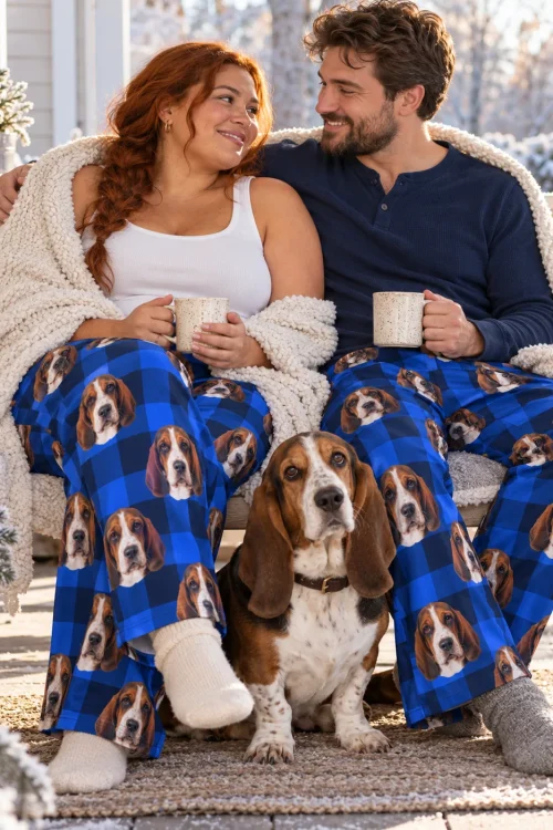 Couple wrapped in a blanket on a snowy porch swing in blue plaid basset hound pajama pants, hound sitting between them
