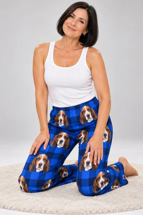 Woman kneeling on a round cream rug, hands on her knees, in blue plaid basset hound pajama pants in a gray studio