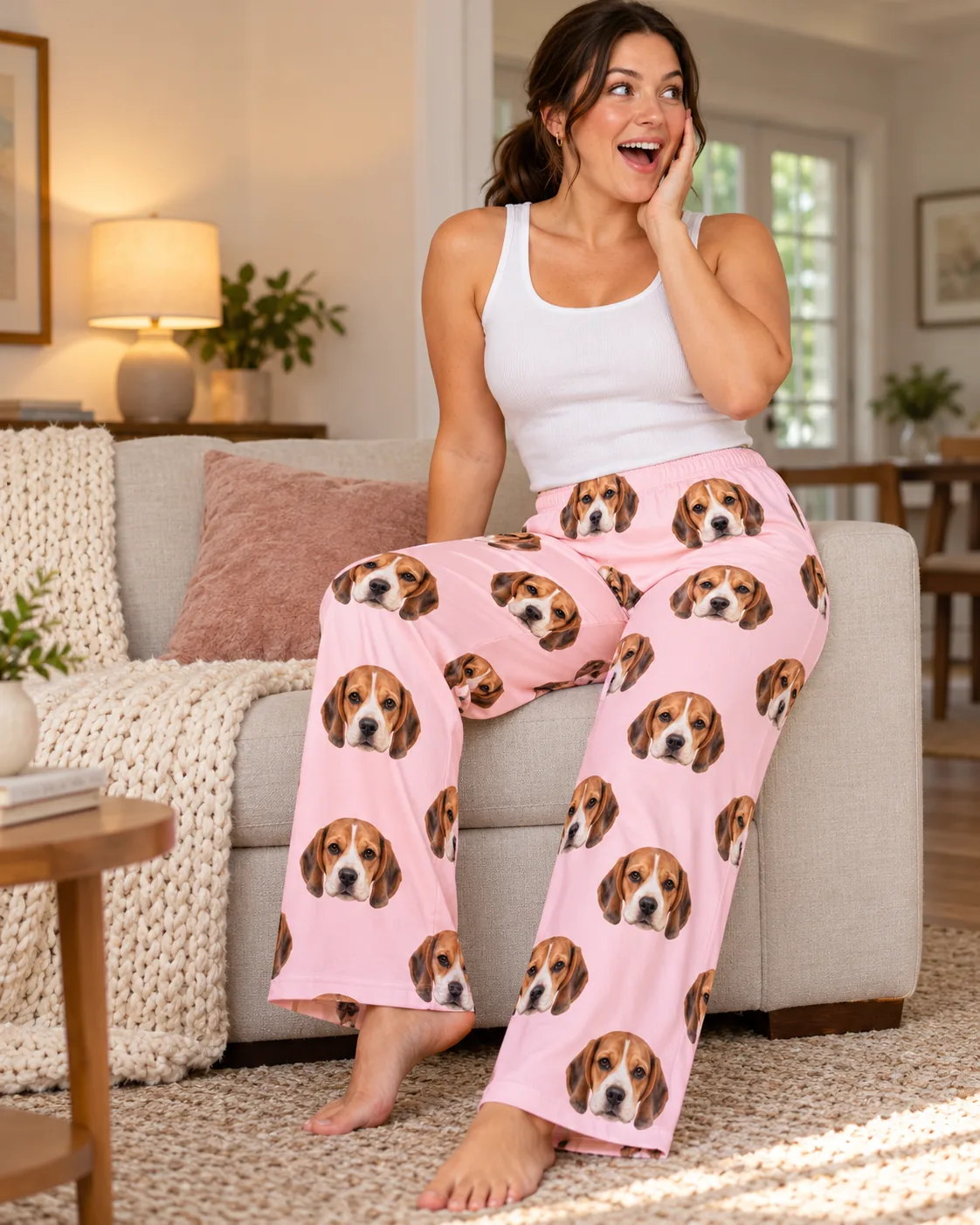Woman on the sofa with a delighted look, in blush pink pajama pants printed with beagle faces