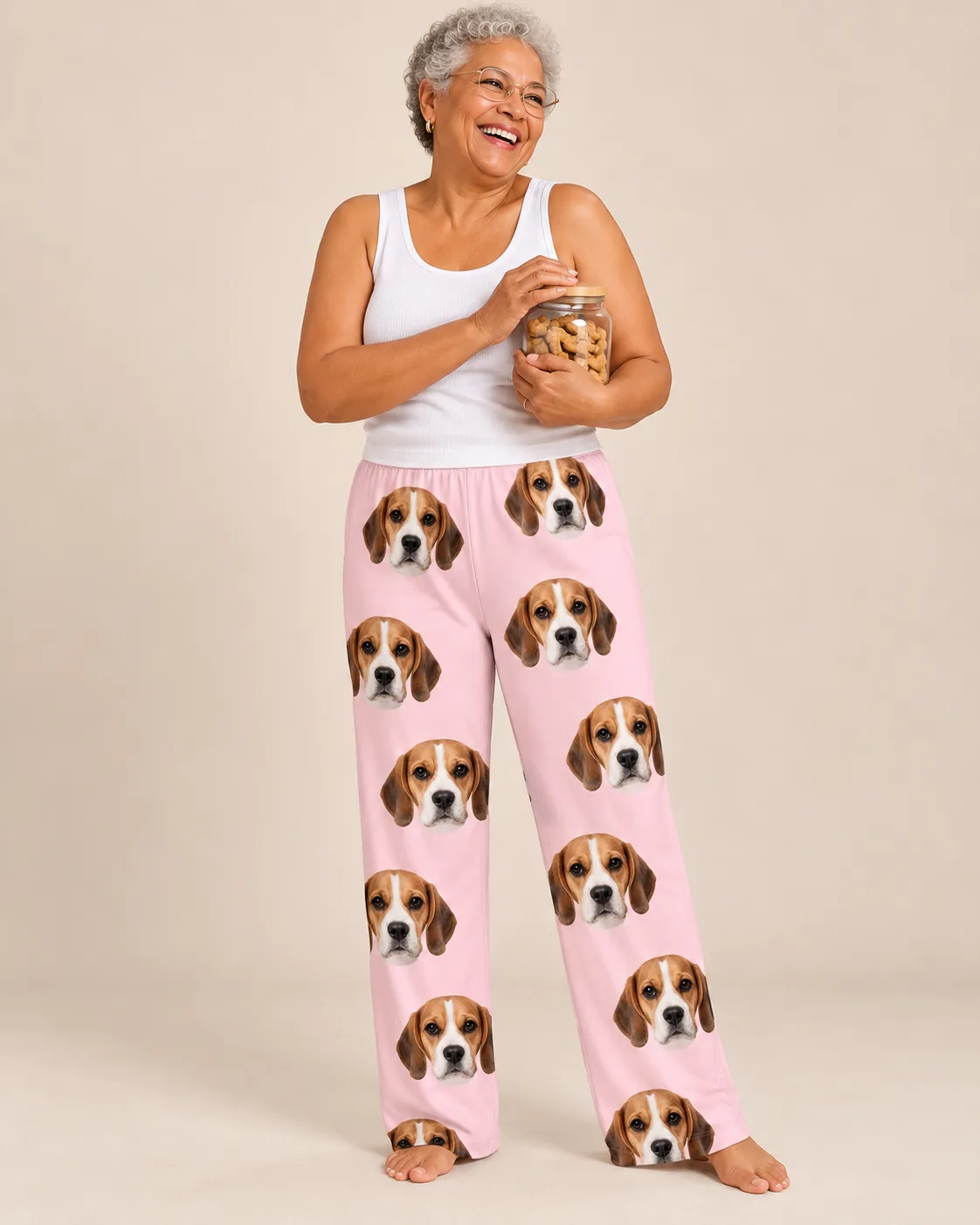 Custom Beagle Pajama Pants for Women — blush pink studio | GenzOutfit Laughing woman hugging a jar of dog treats in blush pink beagle pajamas womens against a tan studio wall