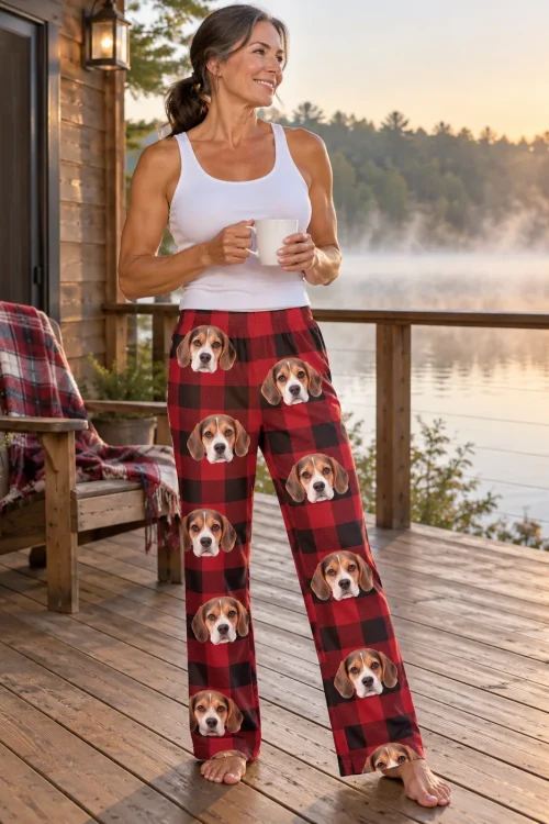 Woman holding a mug on a lake cabin deck at sunrise in red plaid beagle pajama pants