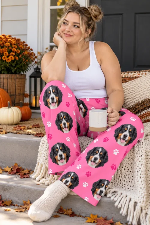 Woman in cozy socks on porch steps among pumpkins and mums, holding a mug, in pink paws Bernese pajama pants