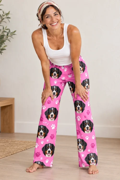 Smiling woman in a white tank top leaning forward in bernese mountain dog pajama pants on pink paws, bright living room