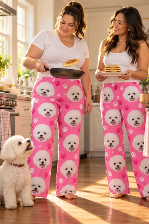 Two women flipping and stacking pancakes in a sunny kitchen in pink paws bichon pajamas, a fluffy bichon begging nearby