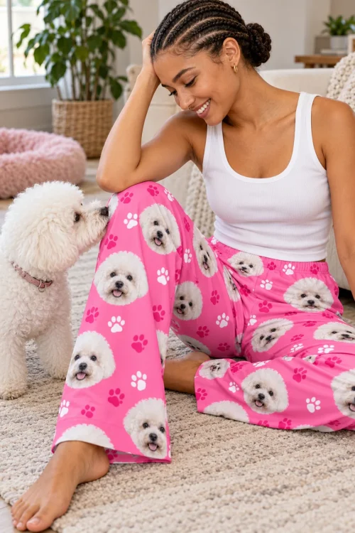 Woman sitting on a cream rug as a white bichon sniffs her knee, in pink paws bichon frise pajama pants