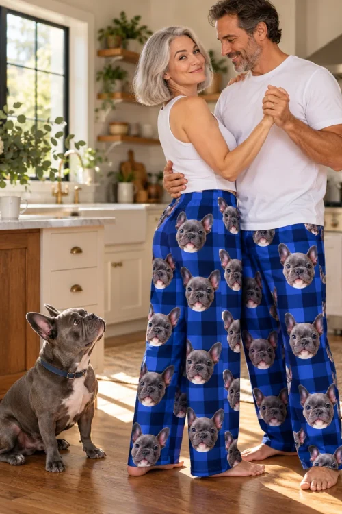 Couple dancing in a kitchen in blue plaid pajama pants with French bulldog faces as their dog watches