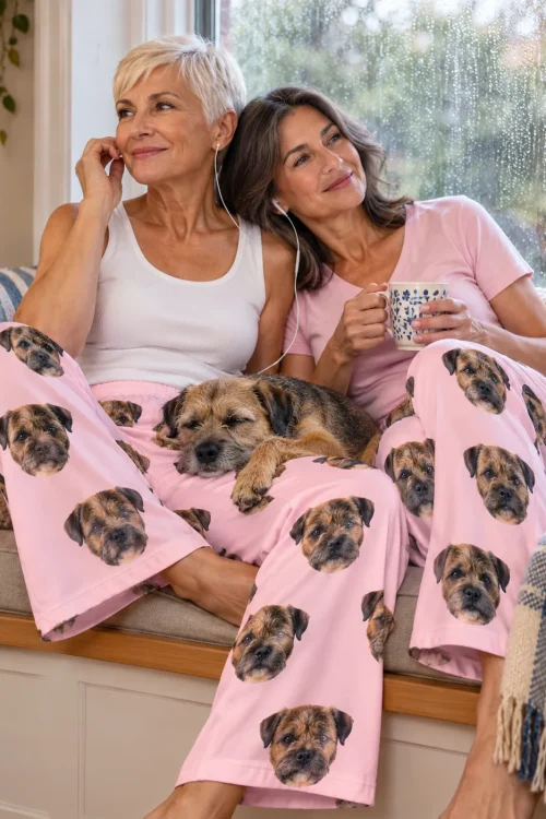 Two women on a rainy window seat with a sleeping border terrier on their laps, both in blush pink pajama pants