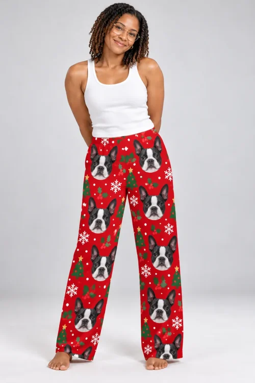 Smiling woman in twists and round glasses standing barefoot in Christmas red Boston terrier pajama pants, gray studio