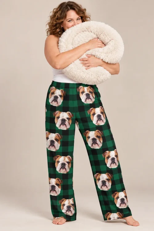 Woman hugging a fluffy dog bed in green plaid bulldog pajama pants against a beige backdrop