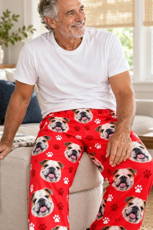 Gray-haired man perched on a sofa arm in red paws bulldog pajama pants
