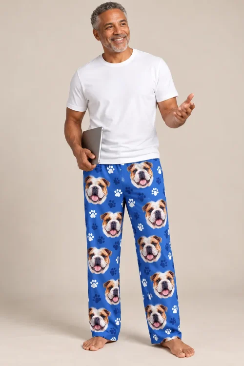 Smiling man holding a tablet in a beige studio, wearing royal blue paws bulldog pajama pants