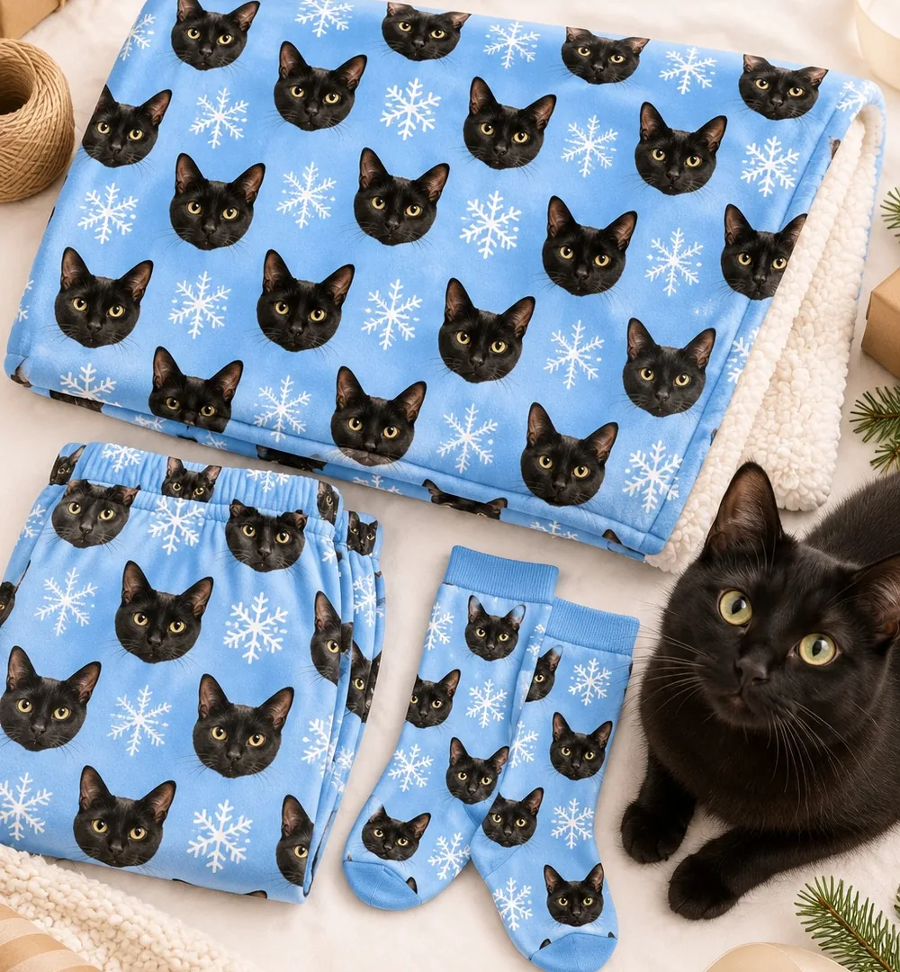 Blue snowflake blanket, pajama pants and socks printed with black cat faces, a black cat lying beside the cat Xmas gift set