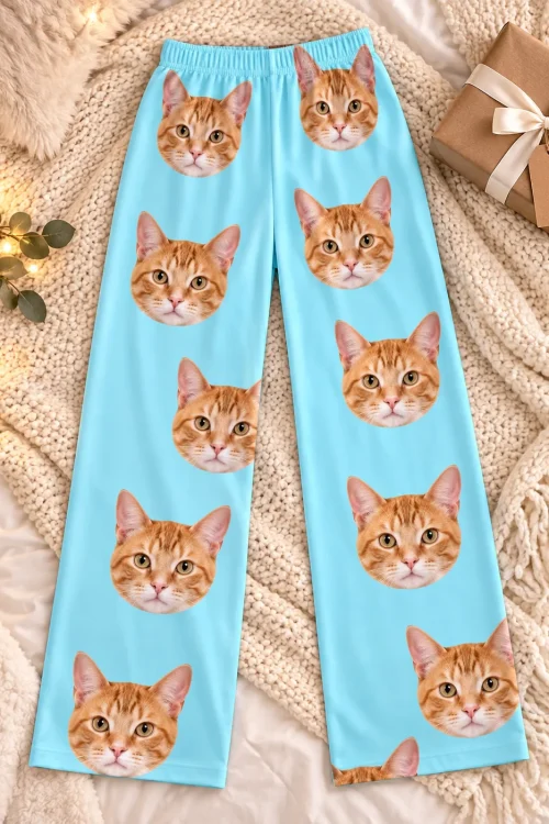 Light blue cat pajama pants with orange tabby faces laid flat on a knit throw beside a gift box