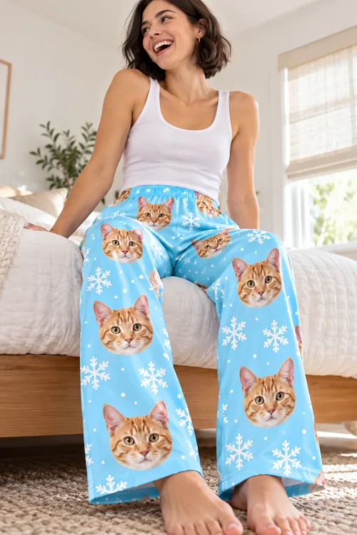 Laughing woman sitting on the edge of her bed in snowflake cat pajama pants with tabby faces