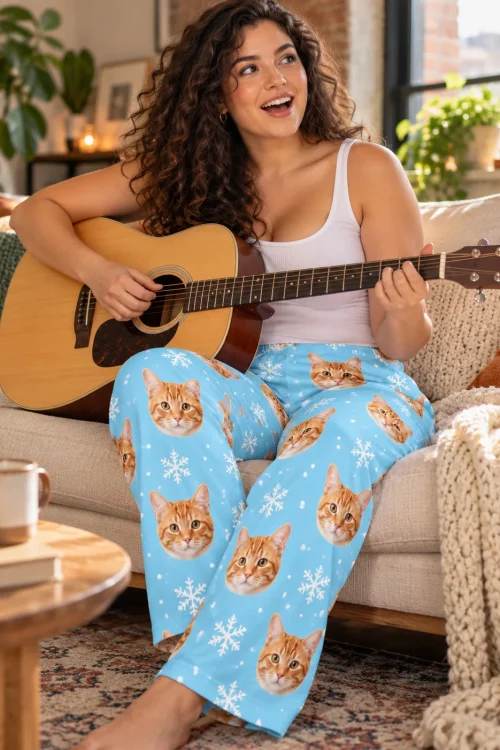 Woman playing an acoustic guitar on the sofa in snowflake cat pajamas with tabby faces