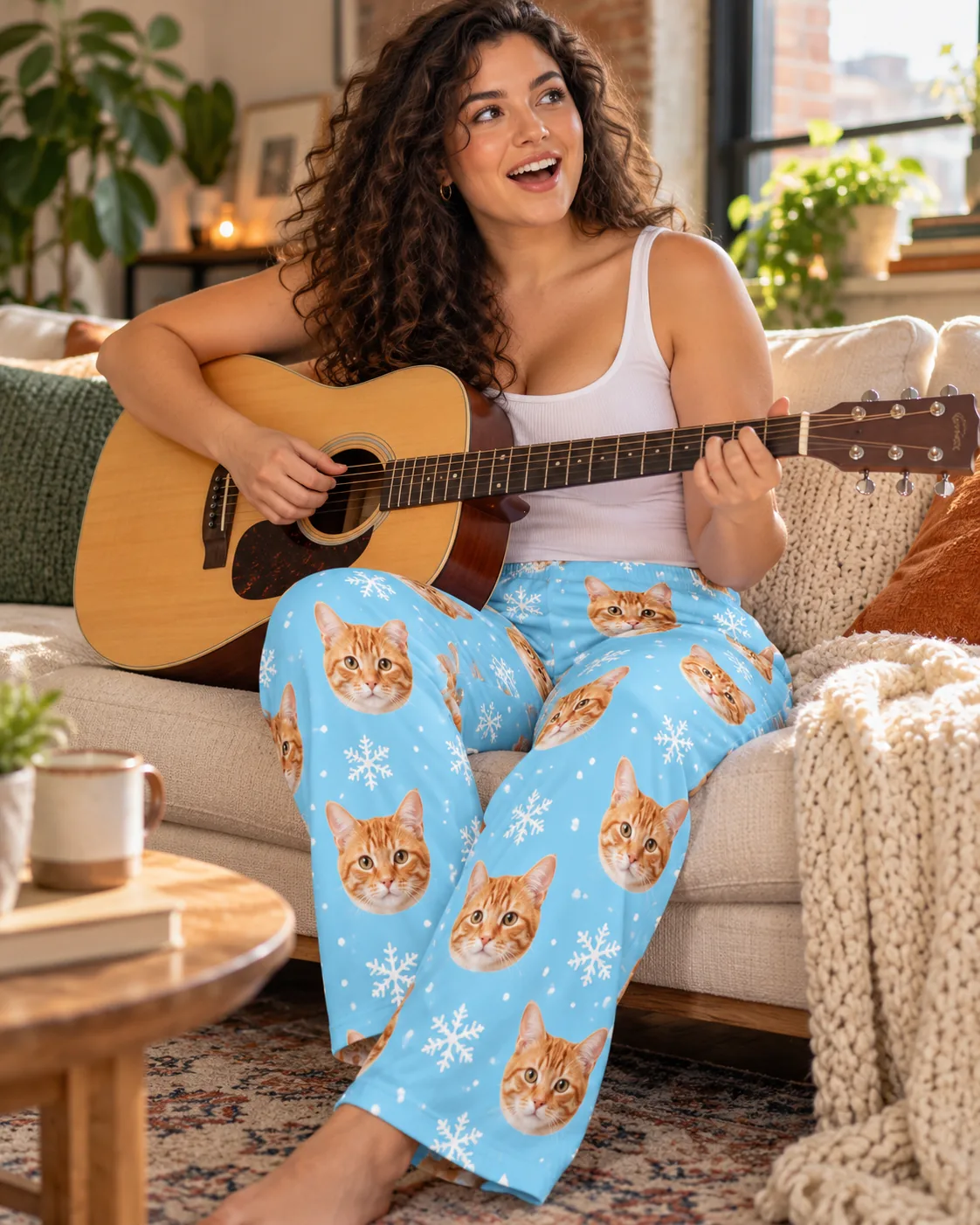 Woman playing an acoustic guitar on the sofa in snowflake cat pajamas with tabby faces