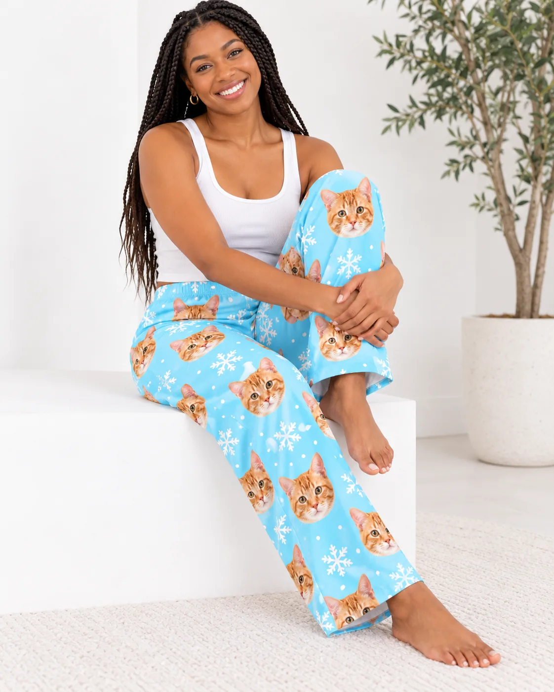 Women's Custom Cat Face Pajama Pants — snowflake studio | GenzOutfit Woman with long braids sitting on a white block in snowflake cat pajamas with tabby faces