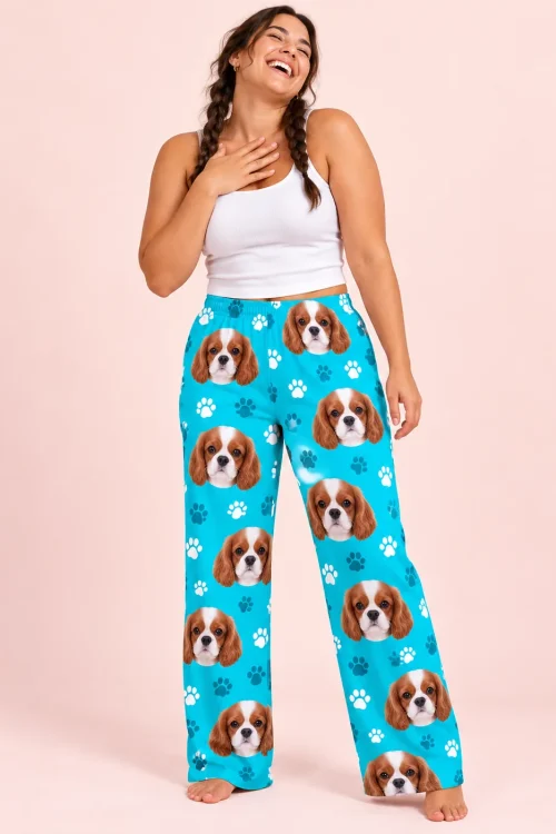 Laughing woman with two braids and a hand on her chest, in teal paws cavalier pajama pants against a blush pink wall