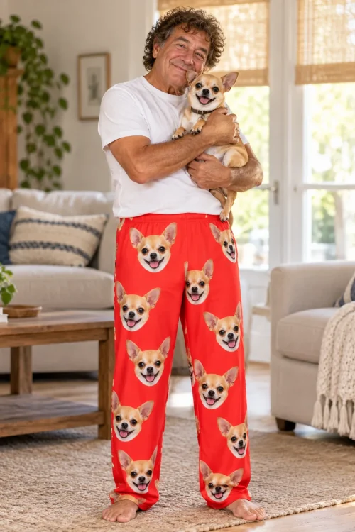 Man holding his chihuahua close in a bright living room, wearing red chihuahua pajama pants