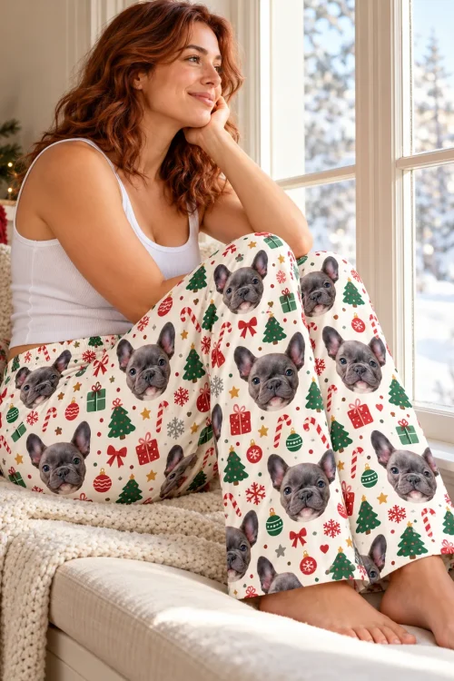 Woman on a window seat with snow outside in Christmas pajama bottoms covered in French bulldog faces