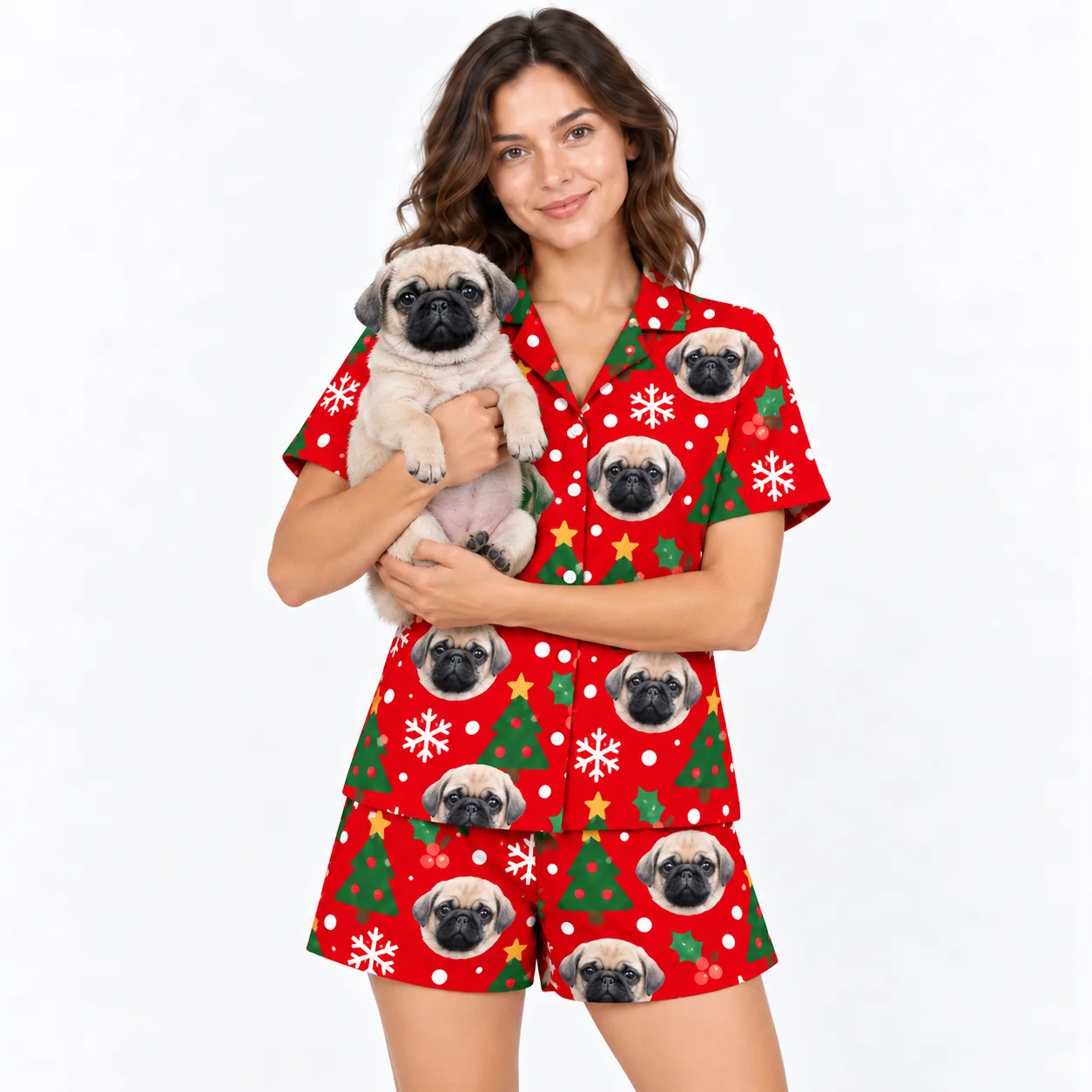 Christmas pajamas with dogs: woman in a red Christmas short set printed with pug faces holding her pug puppy