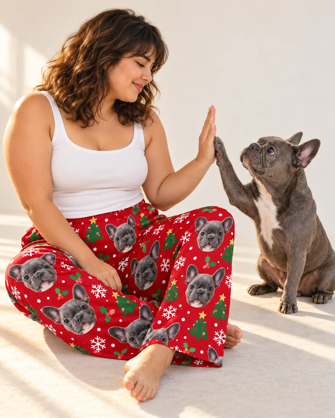 Christmas pajamas: woman in red Christmas pajama pants with French bulldog faces high-fiving her French bulldog