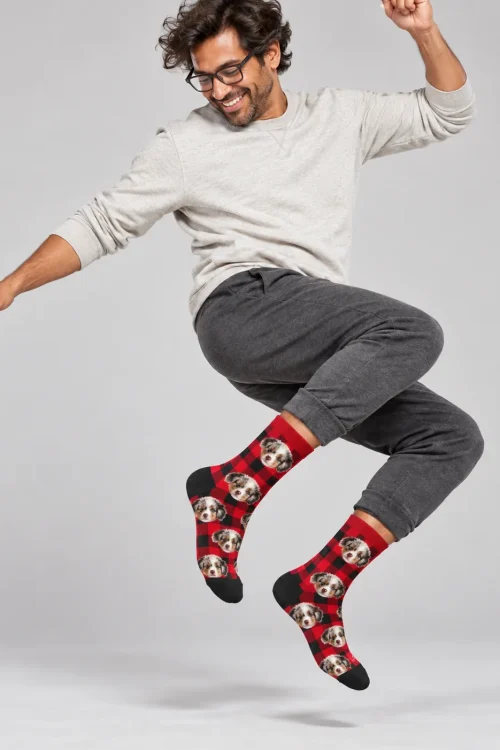 Man jumping mid-air in red plaid Christmas socks with pictures of an Aussie puppy