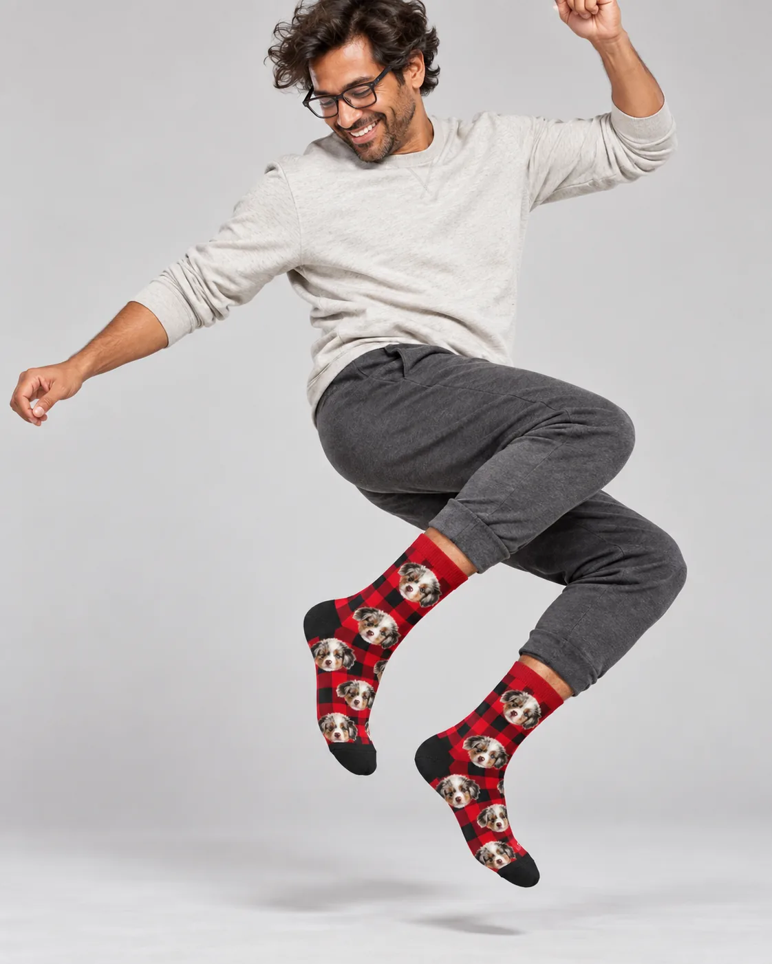 Man jumping mid-air in red plaid Christmas socks with pictures of an Aussie puppy