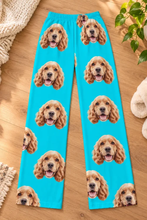 Teal cocker spaniel pajama pants laid flat on a wood floor beside fluffy slippers and a plant