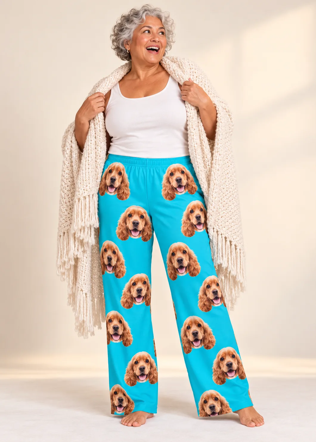 Woman wrapped in a chunky cream shawl in teal cocker spaniel pajama pants, soft studio backdrop