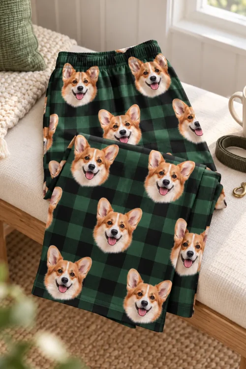 Folded green plaid corgi pajama pants with an elastic waistband on a bench beside a coffee mug and leash