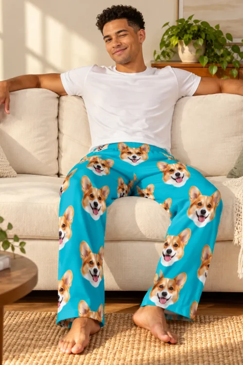 Man winking on a cream sofa in teal corgi pajama pants with corgi faces down both legs