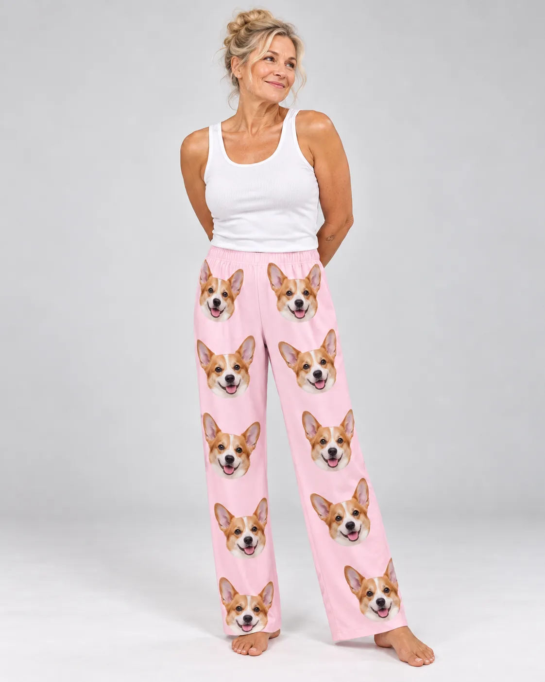 Smiling woman in a white tank and blush pink corgi pajamas for women, barefoot in a light gray studio
