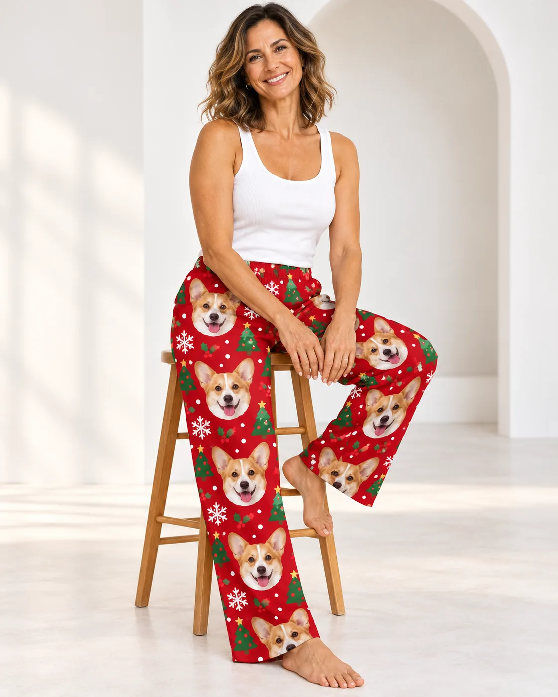 Custom Corgi Pajama Pants for Women — christmas studio | GenzOutfit Smiling woman on a wooden stool in a white studio wearing red Christmas corgi pajamas for women