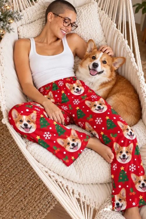 Woman in glasses lounging in a macrame hammock chair with her corgi, in red Christmas corgi pajama pants