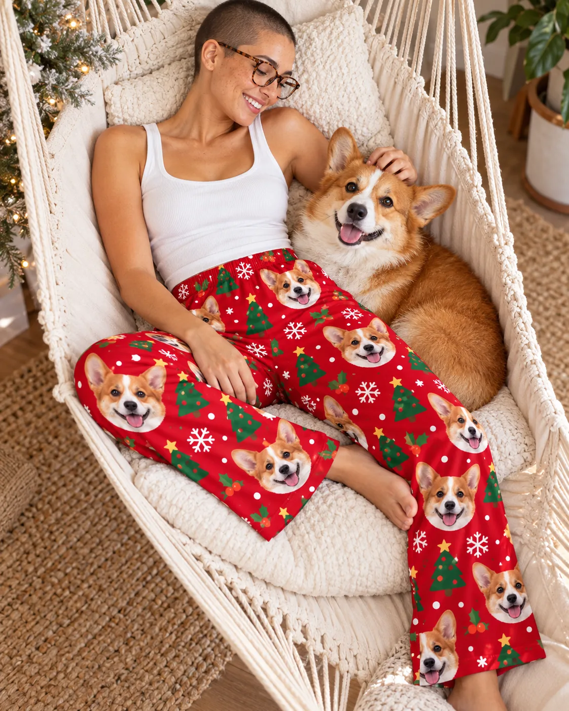Custom Corgi Pajama Pants for Women — christmas with pet | GenzOutfit Woman in glasses lounging in a macrame hammock chair with her corgi, in red Christmas corgi pajama pants