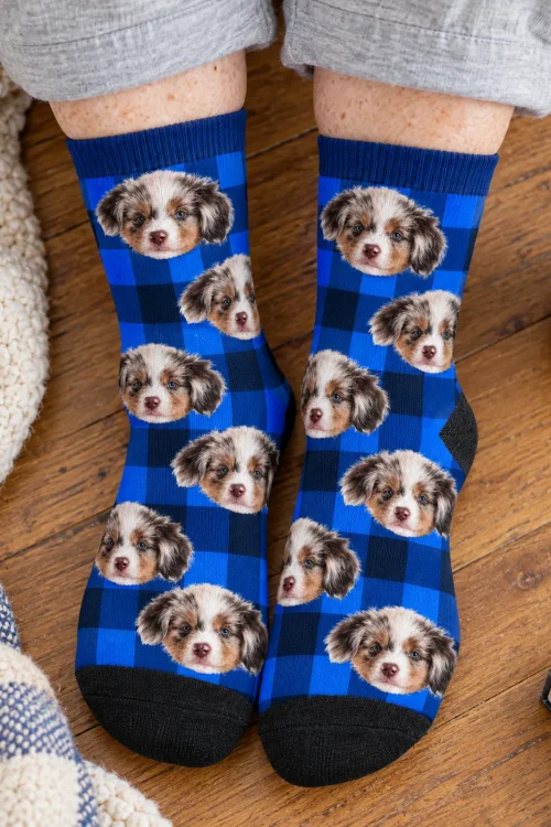 Top-down view of feet on a wood floor in blue and navy plaid socks with puppy faces