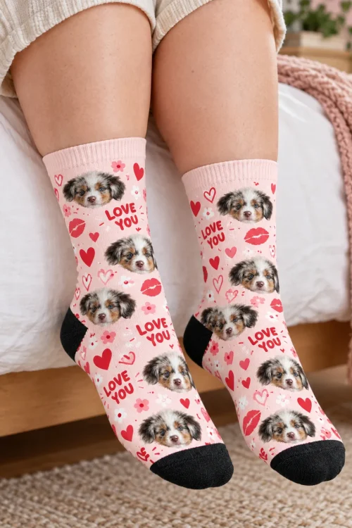 Legs at the edge of a bed in light pink Love You socks with puppy faces and hearts