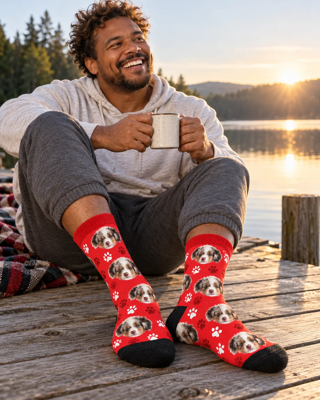 Man with a mug on a lake dock at sunrise in red paw print socks with puppy faces