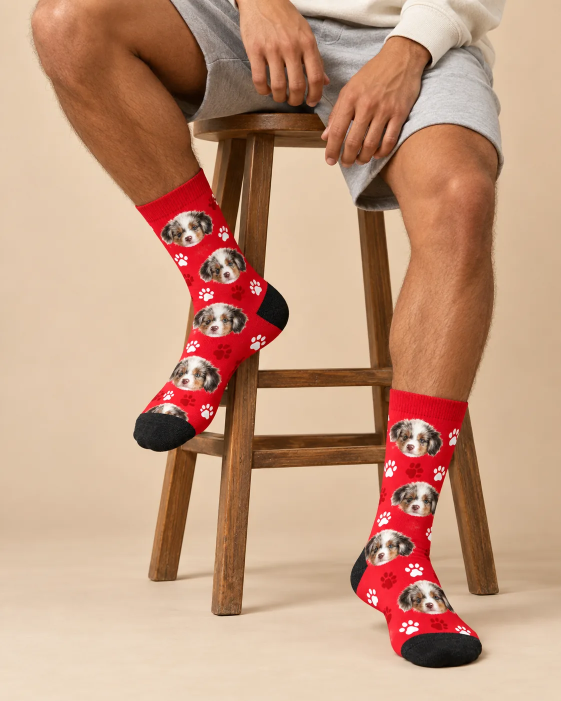 Legs on a wooden stool in red paw print custom socks with multiple puppy faces