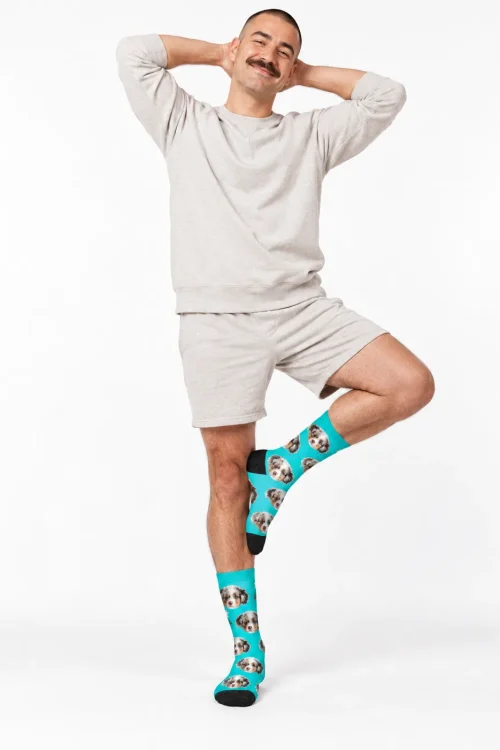 Man balancing in a tree pose wearing teal customized socks with face of an Aussie puppy