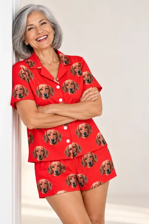 Gray-haired woman leaning on a doorframe in a bright red dachshund pajama set with shirt and shorts