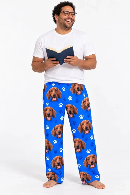 Smiling man in glasses reading a book, wearing royal blue paws men's dachshund pajama pants