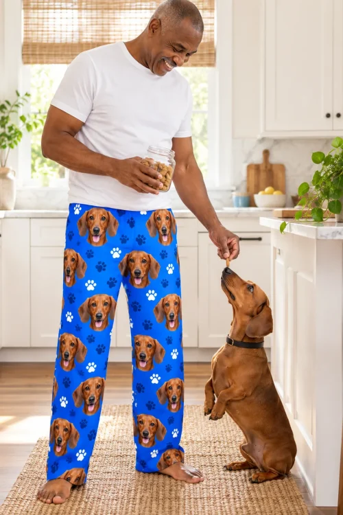 Man offering a treat to his begging dachshund in a bright kitchen, in royal blue paws dachshund pajamas