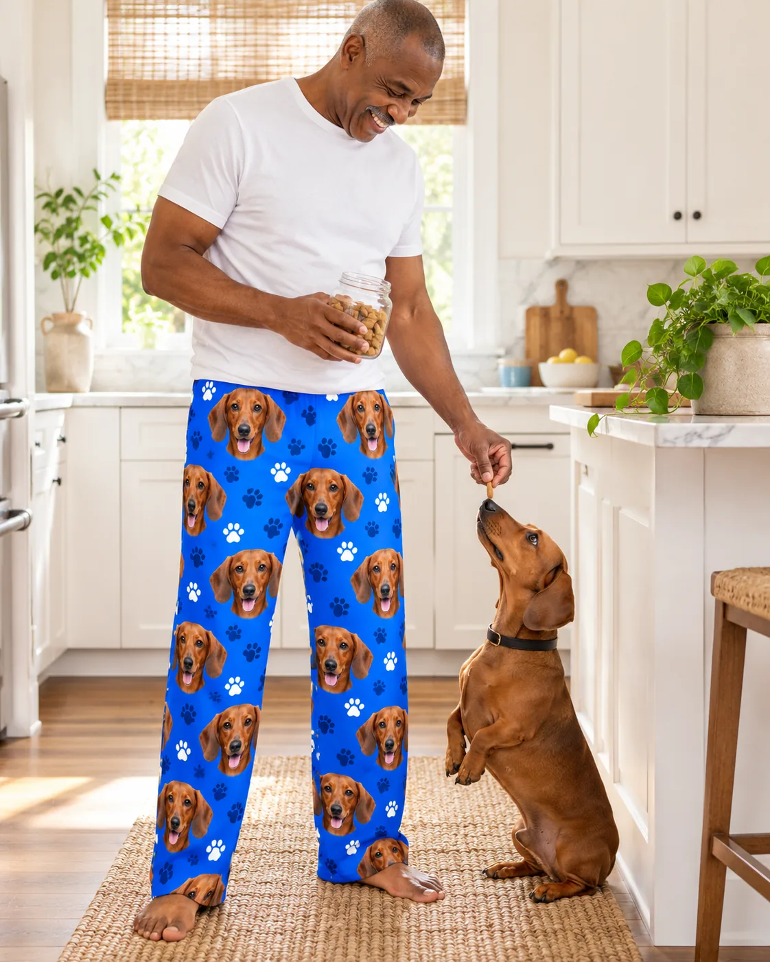 Men's Custom Dachshund Pajama Pants — royal blue paws with pet | GenzOutfit Man offering a treat to his begging dachshund in a bright kitchen, in royal blue paws dachshund pajamas