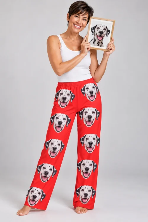 Smiling woman holding a framed dalmatian portrait in red dalmatian pajama pants, light gray studio