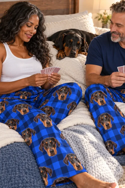 Couple playing cards in bed in blue plaid doberman pajamas while a doberman sleeps behind them